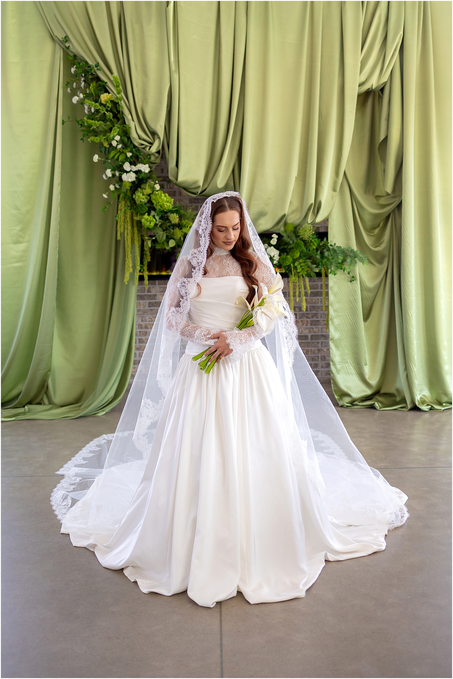 Bride standing in front of green wedding decor while wearing a lace wedding dress and being photographed by the best wedding photographer in South Dakota